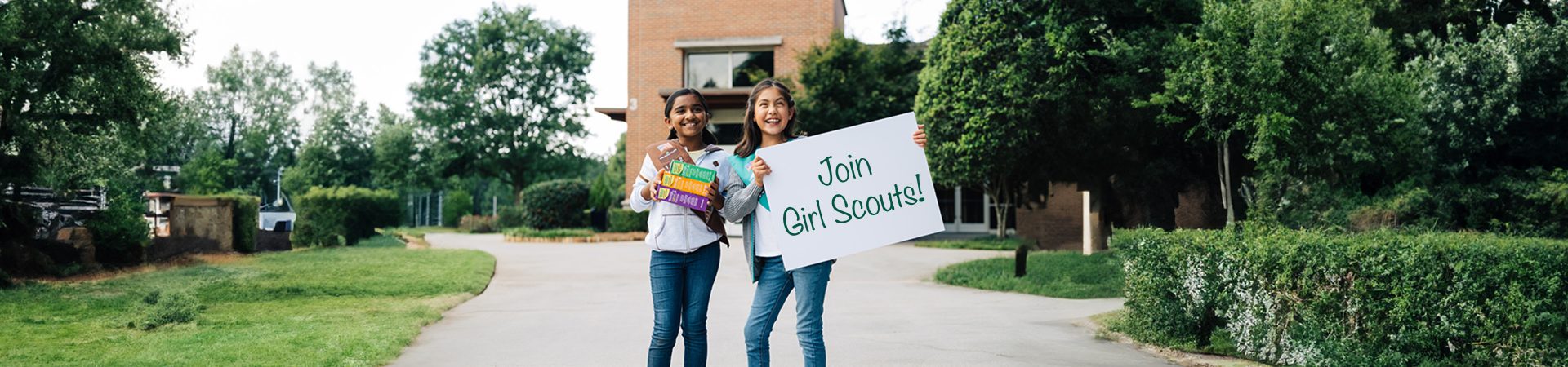  two girls wearing girl scout hoodie and jean jacket hugging and laughing 